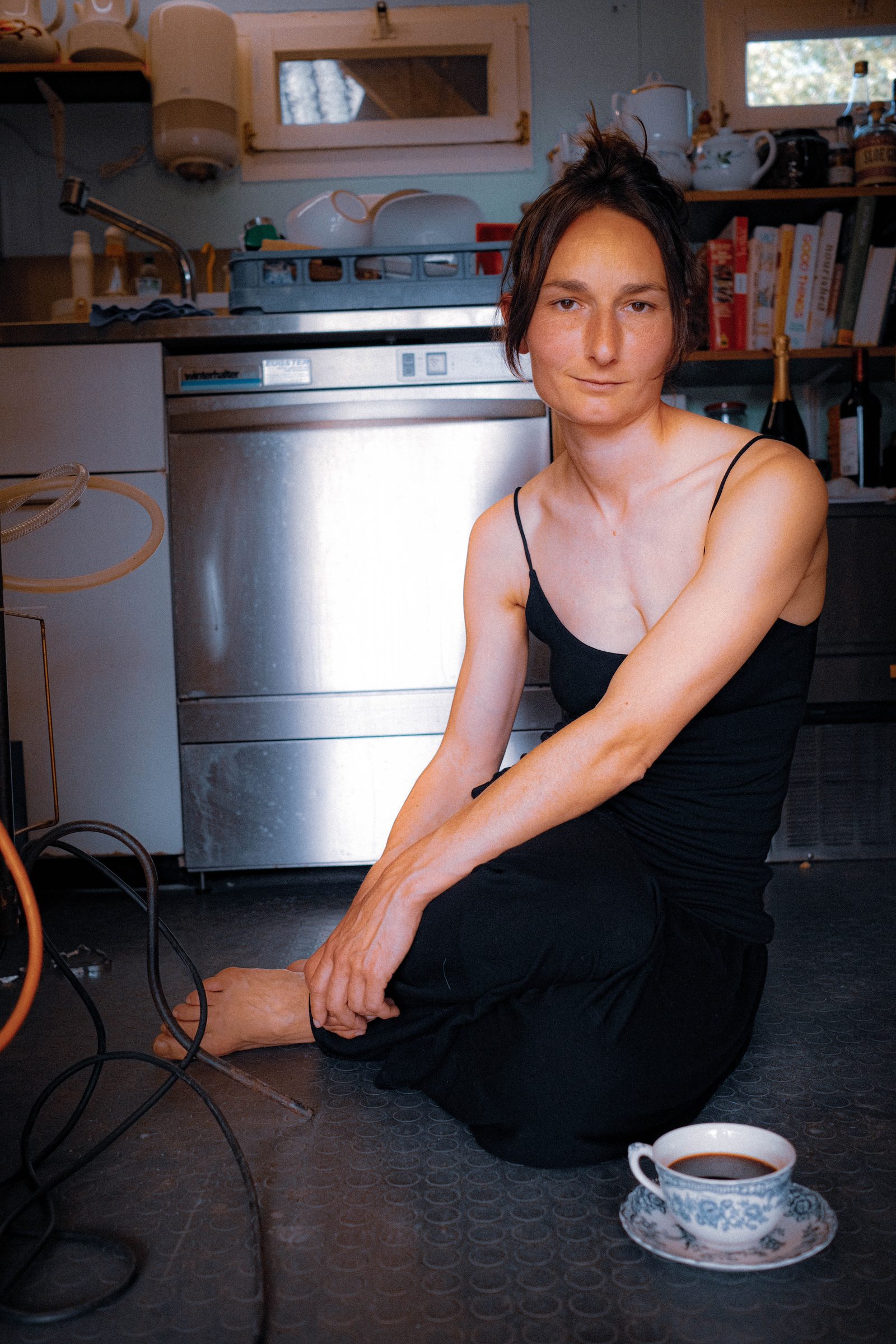 Woman seated on a kitchen floor with a cup of coffee