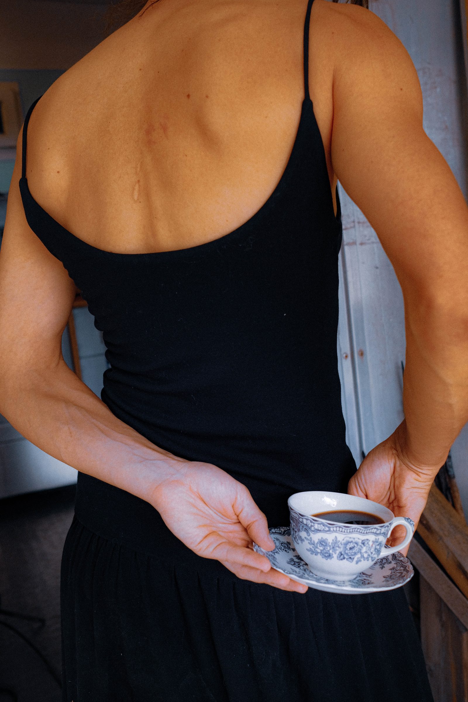 Back of a woman in a black dress holding a teacup