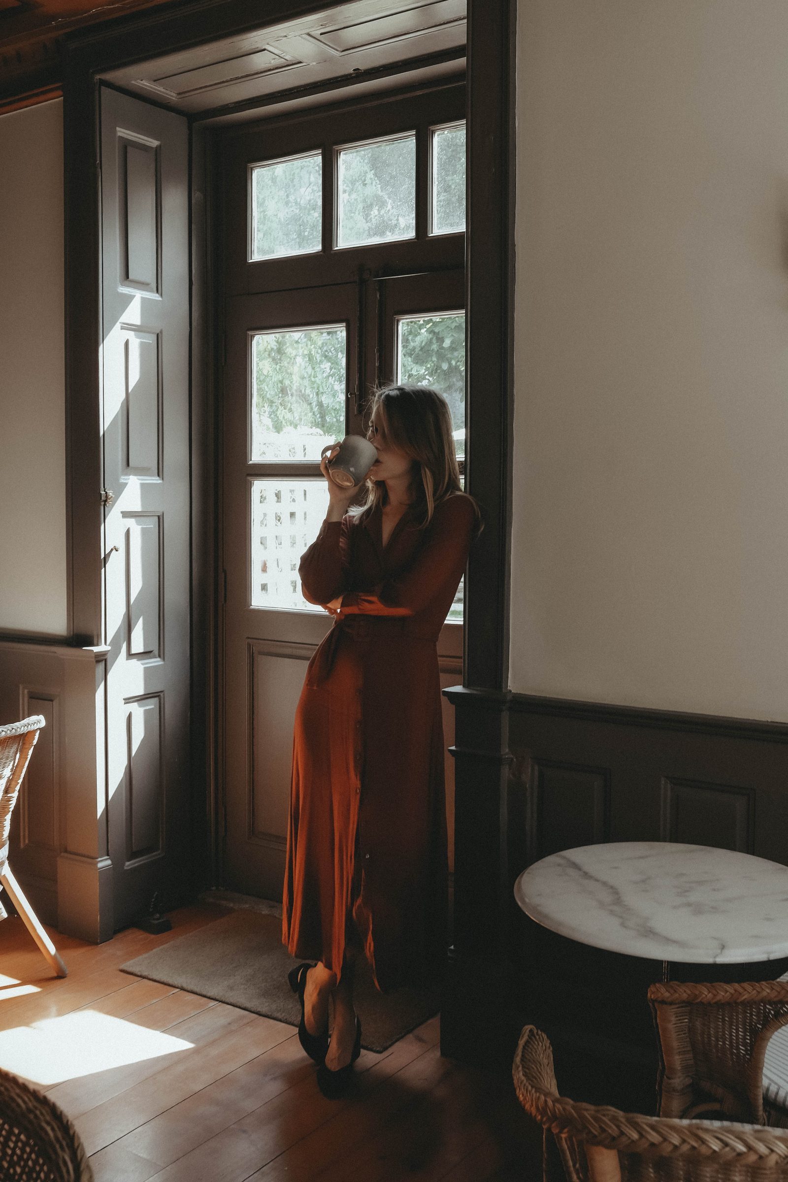 Woman in a rust dress with a camera by a sunlit window
